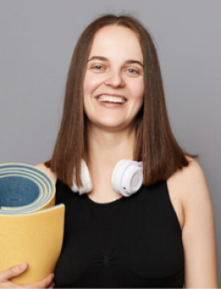 woman in black tank top with headphones around her neck and carrying a yellow yoga mat